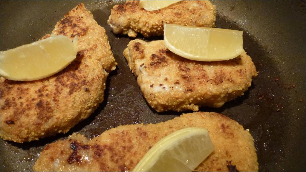 Gluten Free Breaded Pork Chops in a frying pan topped with lemon wedges.