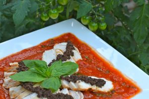 A platter of Chicken with Tapenade and Tomato Basil Sauce garnished with fresh basil.