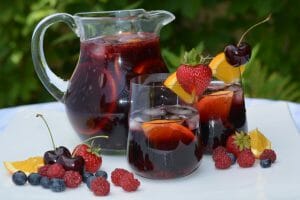 A pitcher and two glasses filled with Prosecco Berry Sangria surrounded by fresh fruit.