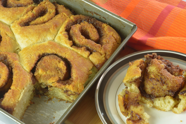 A pan of biscuit cinnamon rolls with one on a plate beside it.