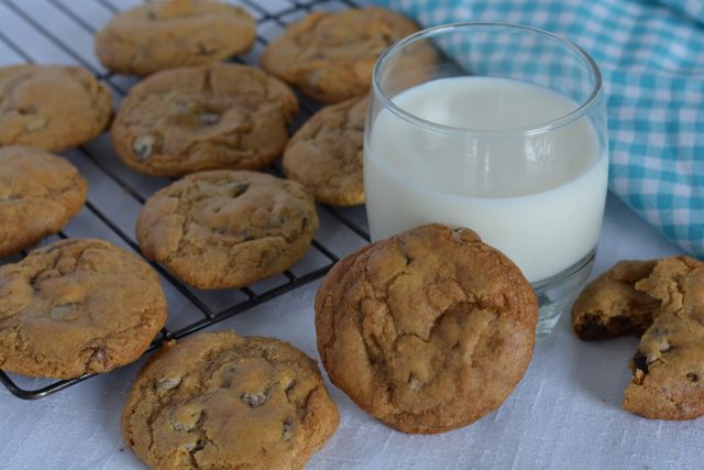 A baking rack of gluten free Chocolate Chip Cookies and a glass of milk.