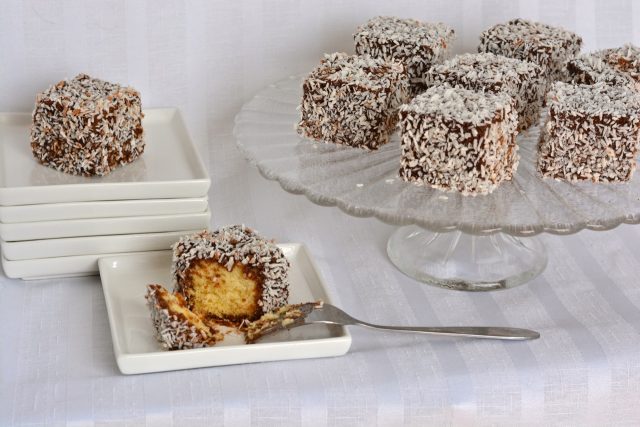 A tray of gluten free lamingtons with one cut and ready to bite into.
