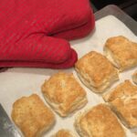 A baking pan of Buttermilk Biscuits with red oven mitts at the side.