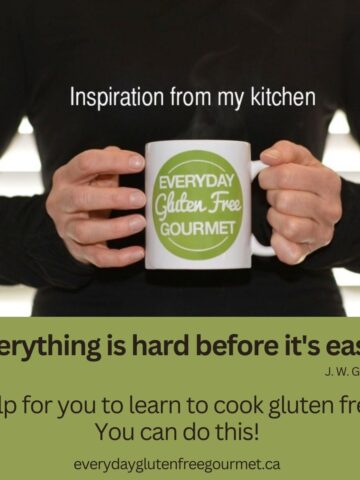 Hands in from of a person in a black sweater holding a steaming cup of coffee with the Everyday Gluten Free Gourmet logo on it.