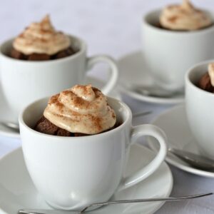 Four tiny espresso cups with gluten free, dairy free cappuccino brownies baked in them, each topped with cinnamon cream cheese.