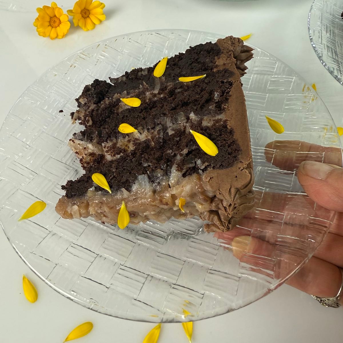 A slice of a three-layered gluten free German Chocolate Cake garnished with calendula flowers and petals.