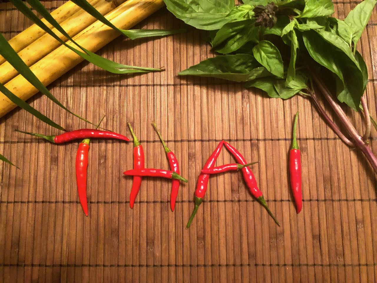 A bamboo placemat with the word THAI spelled using small chili peppers.