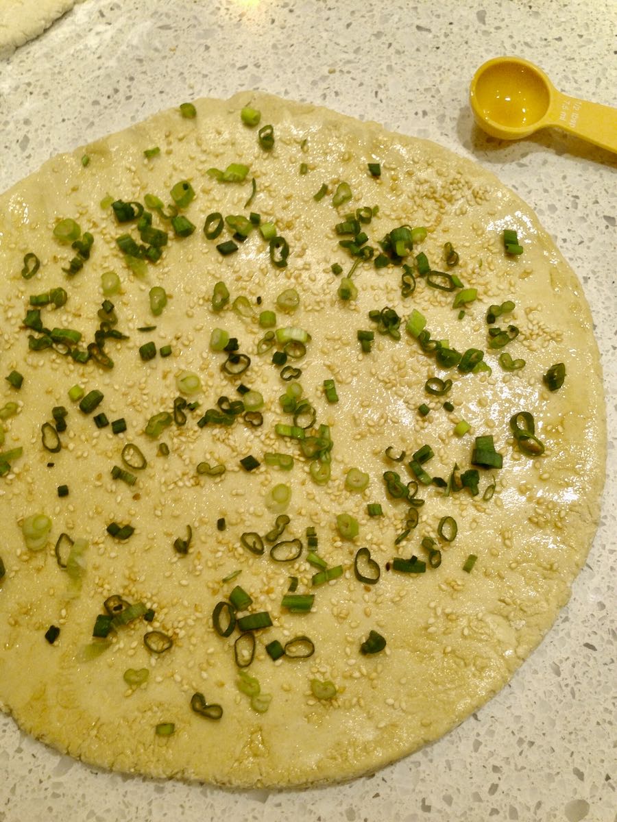 A round of dough for Chinese flatbread topped with green onion, cilantro and sesame seeds.