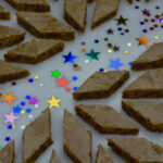 A tray of Cappuccino Cookies cut in diamond shapes decorated with shiny confetti stars.