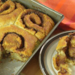 Gluten Free cinnamon rolls in a pan with one on a plate.