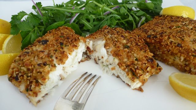 A plate with a gluten free hazelnut lemon halibut filet cut open.