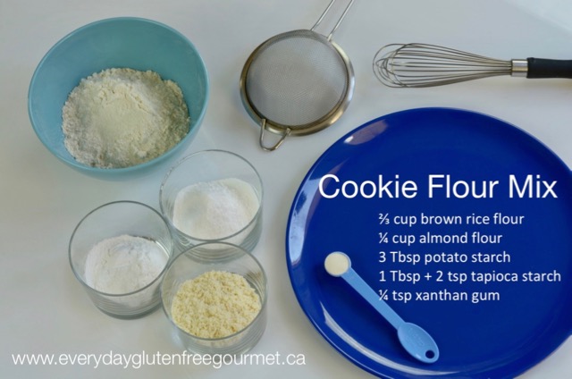 A blue plate with with the recipe in white letters, surrounded by a strainer and 4 bowls with the cookie flour ingredients.