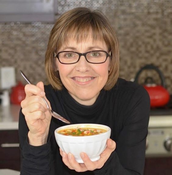 Cinde Little, the Everyday Gluten Free Gourmet, in her kitchen holding a bowl of soup.