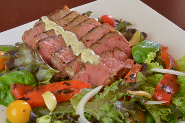 A plate of Blackened Steak Salad with peppers, tomato, onion and blue cheese dressing.