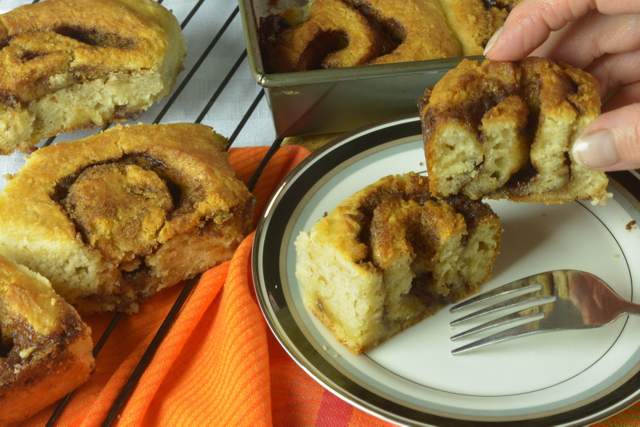 A biscuit cinnamon roll on a plate cut in half, surrounded by other cinnamon rolls in and out of the baking pan.