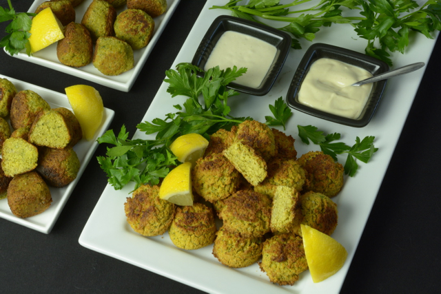 A platter of high fibre Falafel Balls with Tahini Sauce garnished with fresh parsley and lemon wedges.