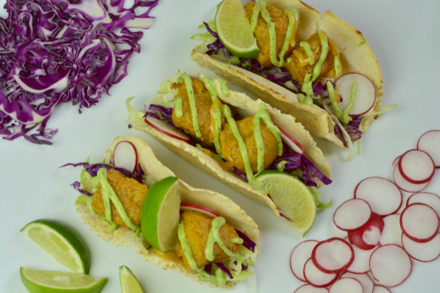 Fish tacos with avocado crema and lime surrounded by shredded purple cabbage and sliced radishes.