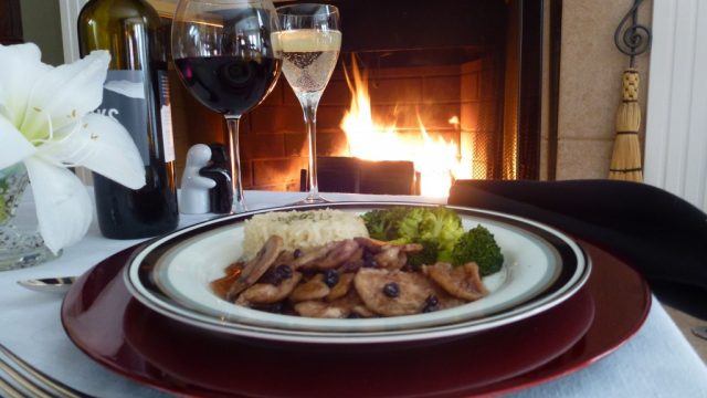 A plate of gluten free Chicken Porto with rice pilaf and broccoli on a table set in front of a fireplace.