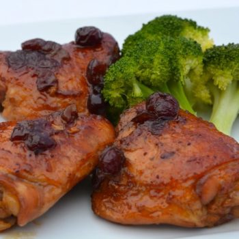 Three chicken thighs on a plate with Cranberry Orange sauce and cooked broccoli.