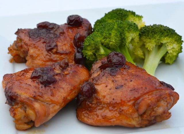 Three chicken thighs on a plate with Cranberry Orange sauce and cooked broccoli.