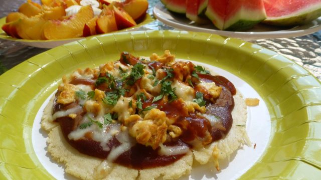 A paper plate with homemade soft corn tortillas topped with enchilada sauce, scrambled eggs and cheese, a hearty Mexican Huevos Rancheros.