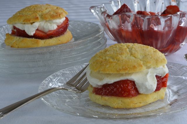 Gluten Free Strawberry Shortcake on a plate filled with strawberry sauce and whipped cream, with more in the background.