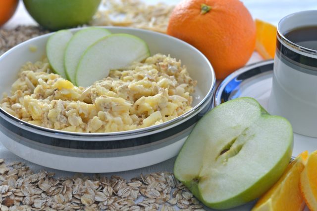 A shallow bowl of overnight oats with slices of apple and a whole orange beside it.