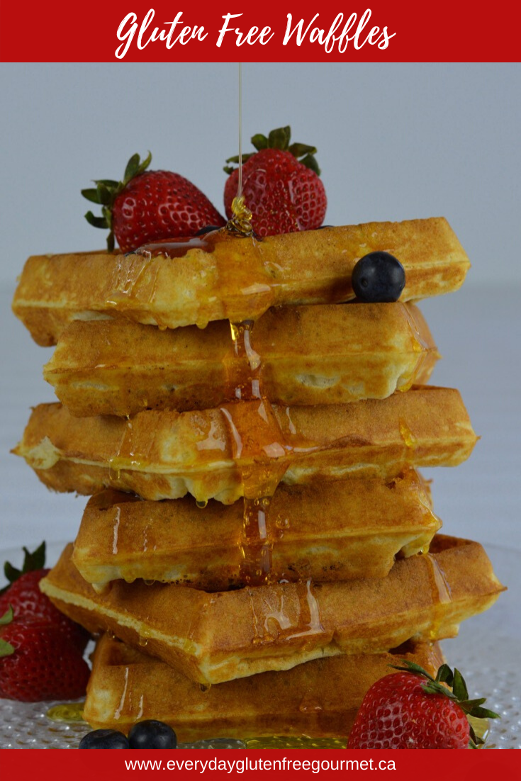 A pile of Gluten Free Waffles with strawberries and blueberries, and corn syrup drizzling all the way down.