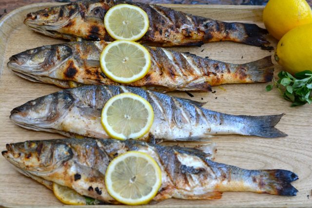 Whole Grilled Branzino right off the barbecue garnished with lemon slices.