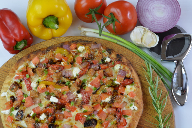 A close up of Gluten free Grilled Sausage and Vegetable Pizza surrounded by peppers, tomatoes and onion.