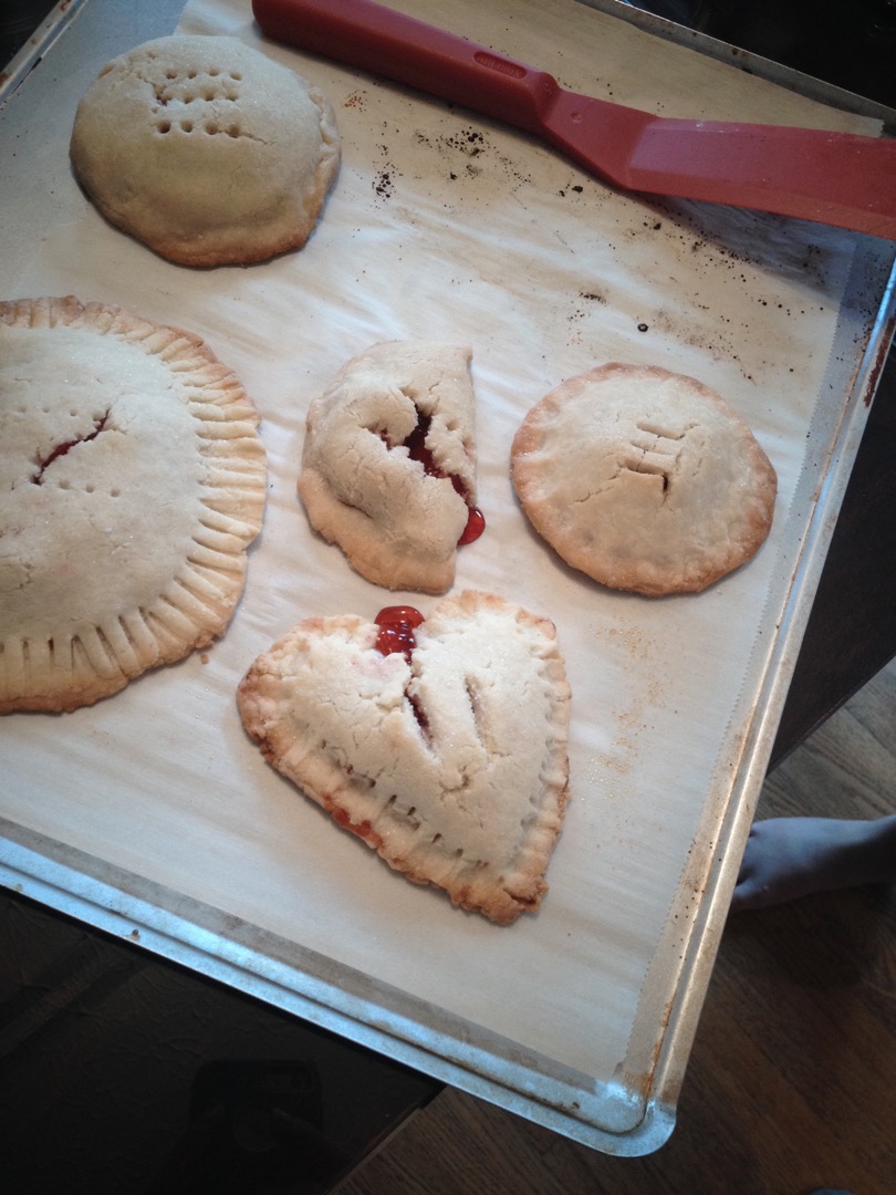 A heart shaped Cherry Hand Pie and some rounds ones on a baking sheet.