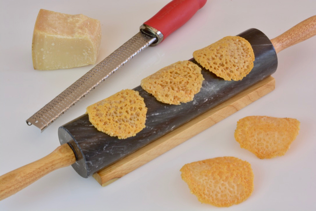 Parmesan Cheese Wafers laying on a rolling pin to cool with Parmesan cheese and a grater beside them.