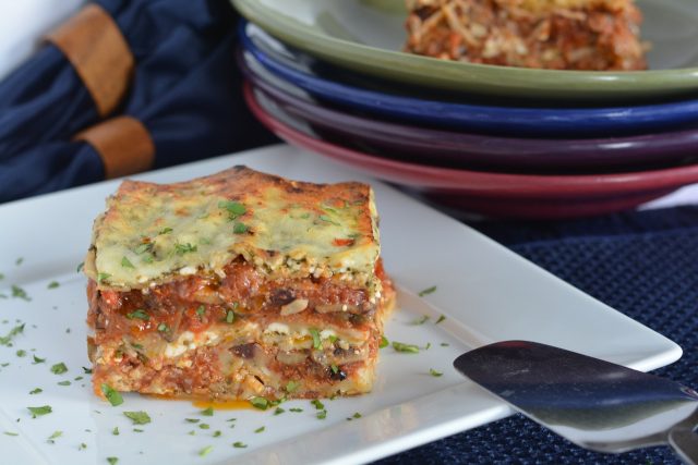 A piece of pesto lasagna sprinkled with parsley sitting beside a stack of colourful bowls.