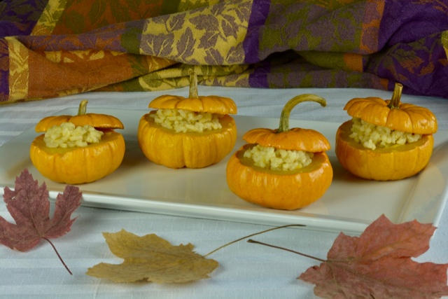 A plate of mini pumpkins filled with Pumpkin Risotto with fall leaves on the table in front of them.