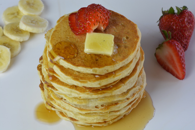 A stack of pancakes with butter and syrup ready to cut into.