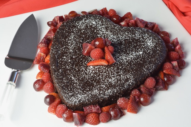 Heart shaped Quinoa Chocolate Cake surrounded by red fruit; strawberries, raspberries and red grapes. 