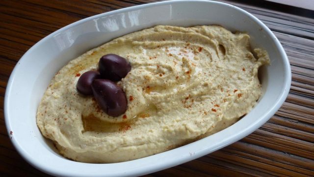 A dish of gluten free lemony hummus topped with a drizzle of olive oil