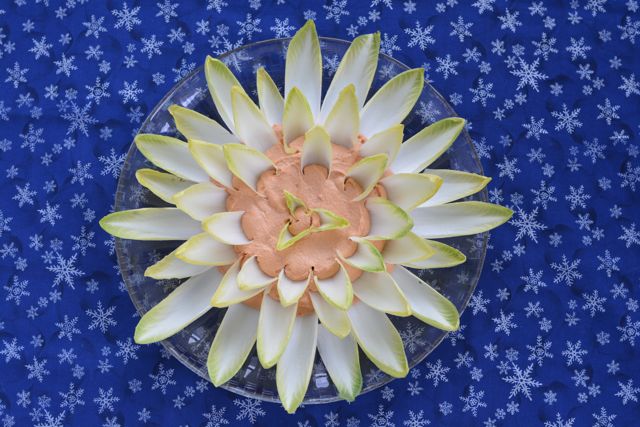 A platter of smoked salmon pate with belgain endive leaves poked into the pate in and around it.