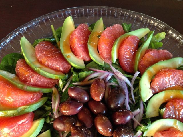 A composed Grapefruit Avocado Salad with olives and red onion in the center.