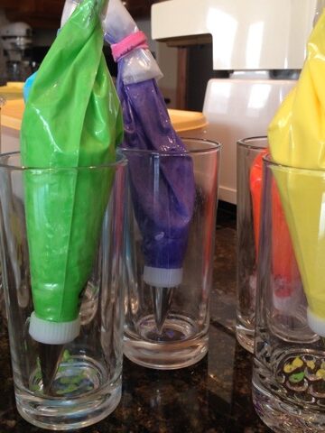 Drinking glasses holding piping bags with different colours of royal icing.