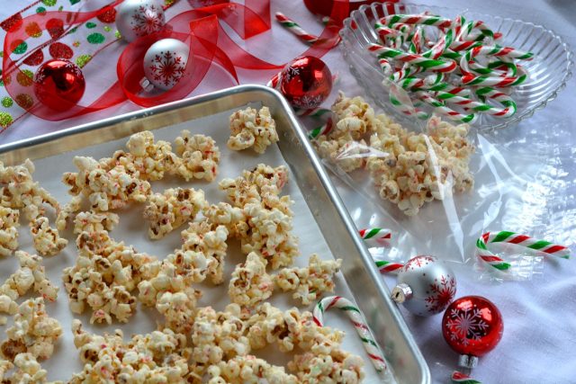 A pan with clumps of White Chocolate Candy Cane Popcorn beside the gift bags, candy canes and ribbon ready for gift wrapping.