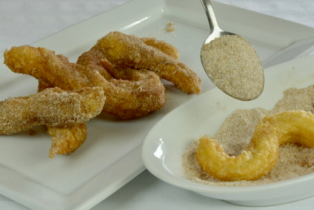 Sprinkling cinnamon-sugar on freshly deep-fried churros.