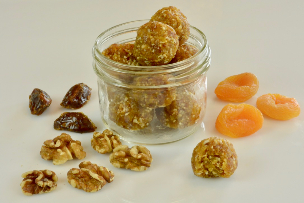 Coconut Date Energy Balls in a Mason jar surrounded by dates, apricots and walnuts.
