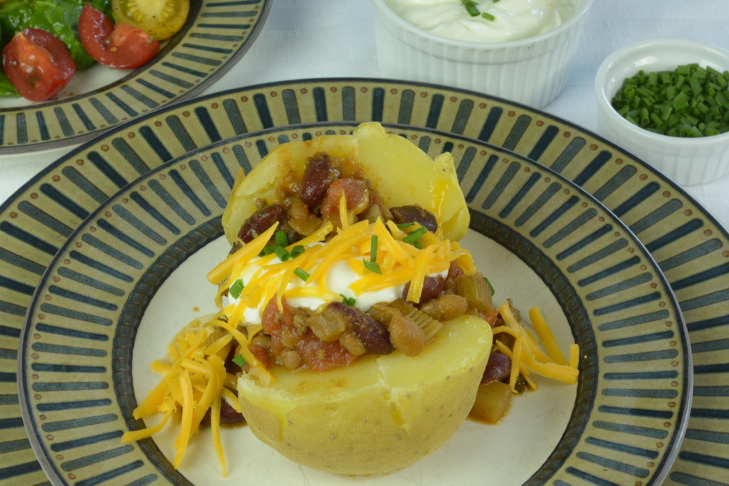A Baked Potato topped with Chili, sour cream, cheddar cheese and chives.