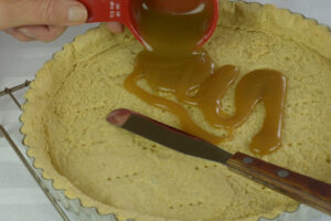 A cooked tart pastry shell with bourbon caramel sauce being poured on it.