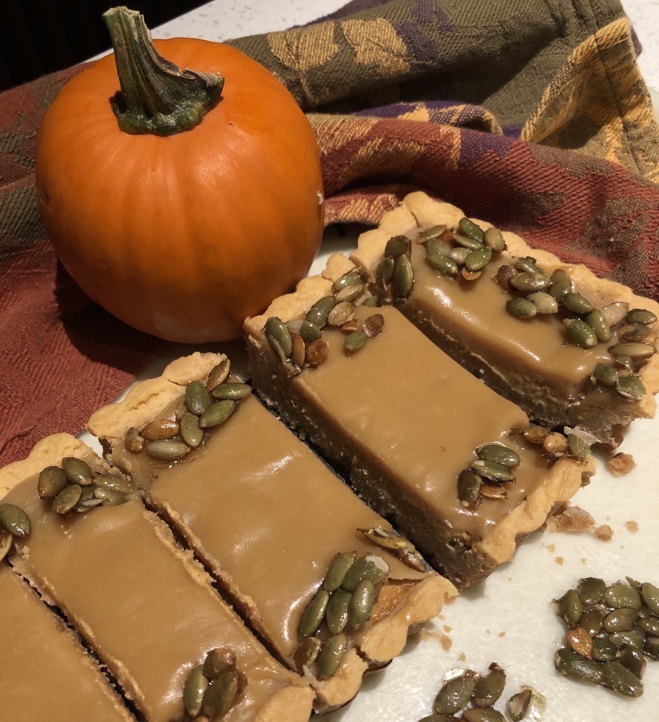 A rectangular shaped Bourbon Caramel Pumpkin Tart with an autumn coloured napkin and a mini sugar pumpkin.