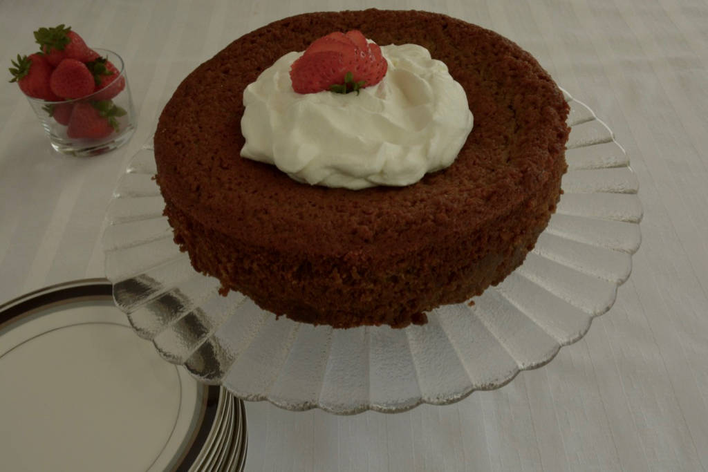 A round Sticky Date Pudding  on a pedestal cake stand topped with whipped cream and strawberries.