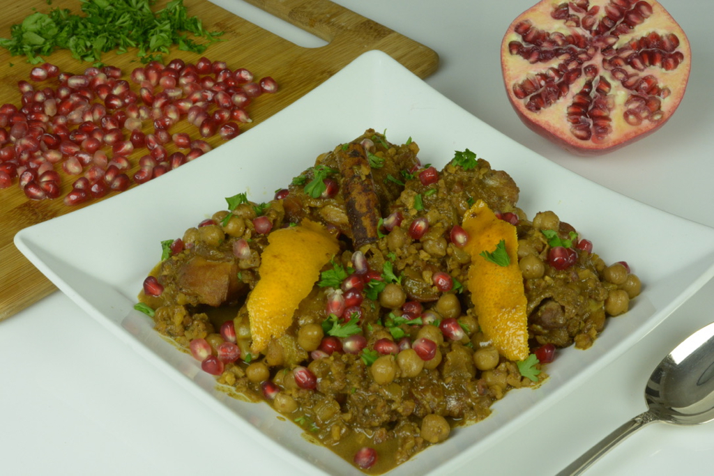 A white plate of Persian Chicken Stew sprinkled with pomegranate arils.