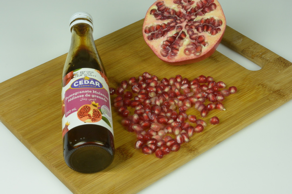 A cutting board with half a pomegranate beside a bottle of pomegranate molasses.