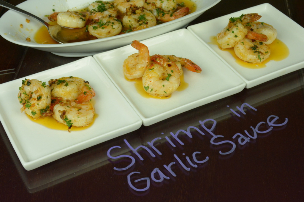 Three small plates each with three shrimp in garlic sauce to be served.